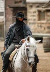 Naamioitu cowboy ratsastaa valkoisella hevosella villin lännen kadulla