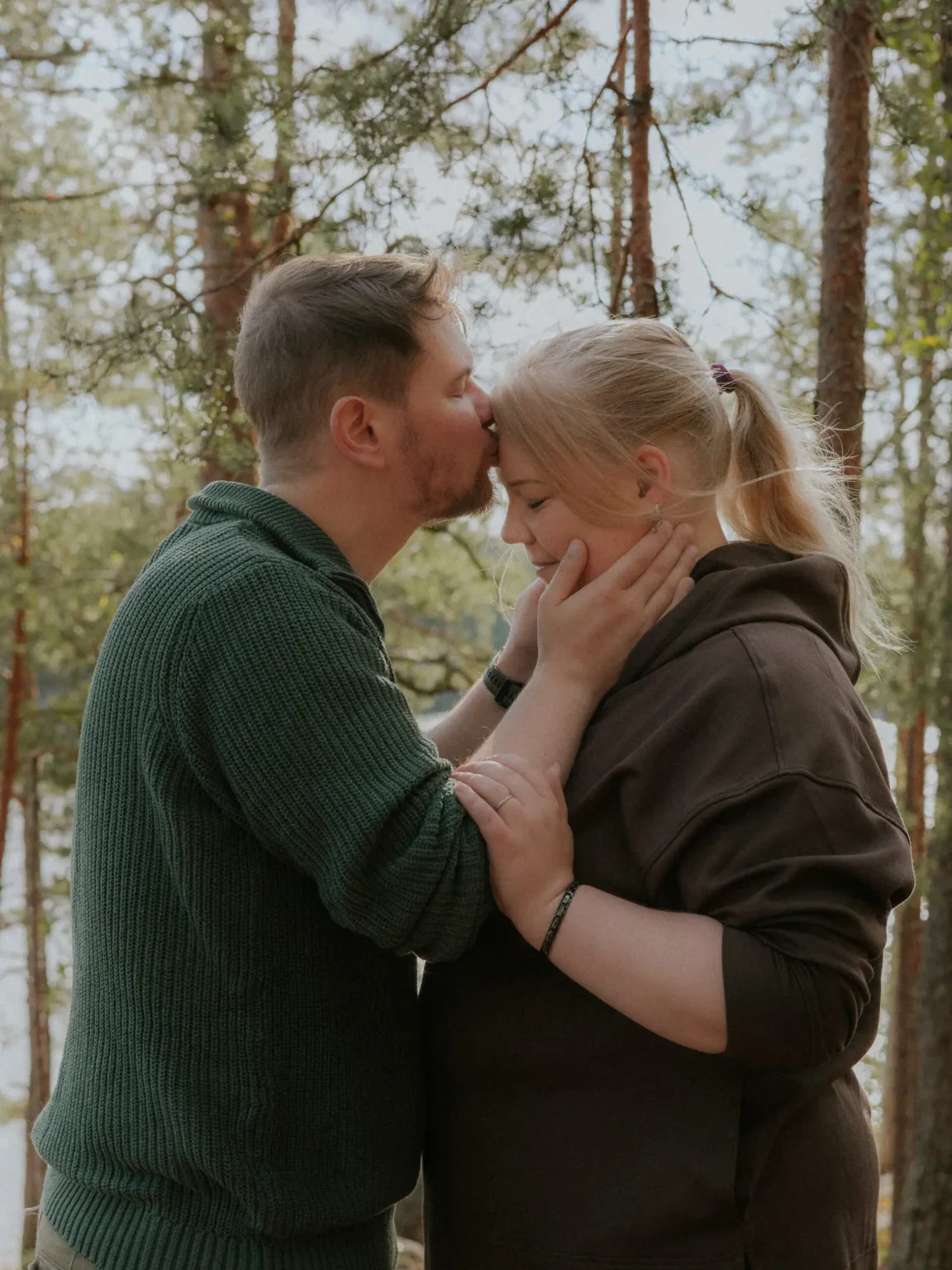 Mies suukottaa naisen otsaa metsässä