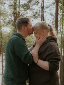 Mies suukottaa naisen otsaa metsässä