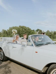 Hääpari vilkuttaa valkoisesta avoautosta